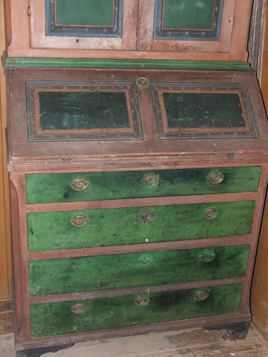 Todelt skap i tre. To skapdører øverst, 8 små skuffer i midten og fire større skuffer nederst. Oppheng til skjeer i øverste skap. Utskjæringer i tre øverst. Grønnmalte fyllinger dekorert med små blomster.