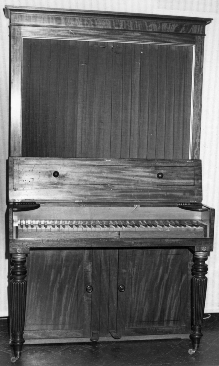 Instrument med omfang: FF - f'''' (6 oktaver).

Firkantet korpus med to bein framme og en rød tekstilavdekking på forsiden. Finer sannsynligvis mahagoni. Lokk tredelt med to knapper og mørk treinnlegg. Når lokket åpnes kan to halvsirkelformede plater felles frem som hyller for lysestaker.
Under klaviatur to dører foran klangbunnen.