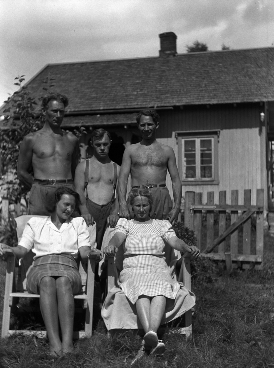 Ukjente kvinner og menn i en hage foran et hus. 