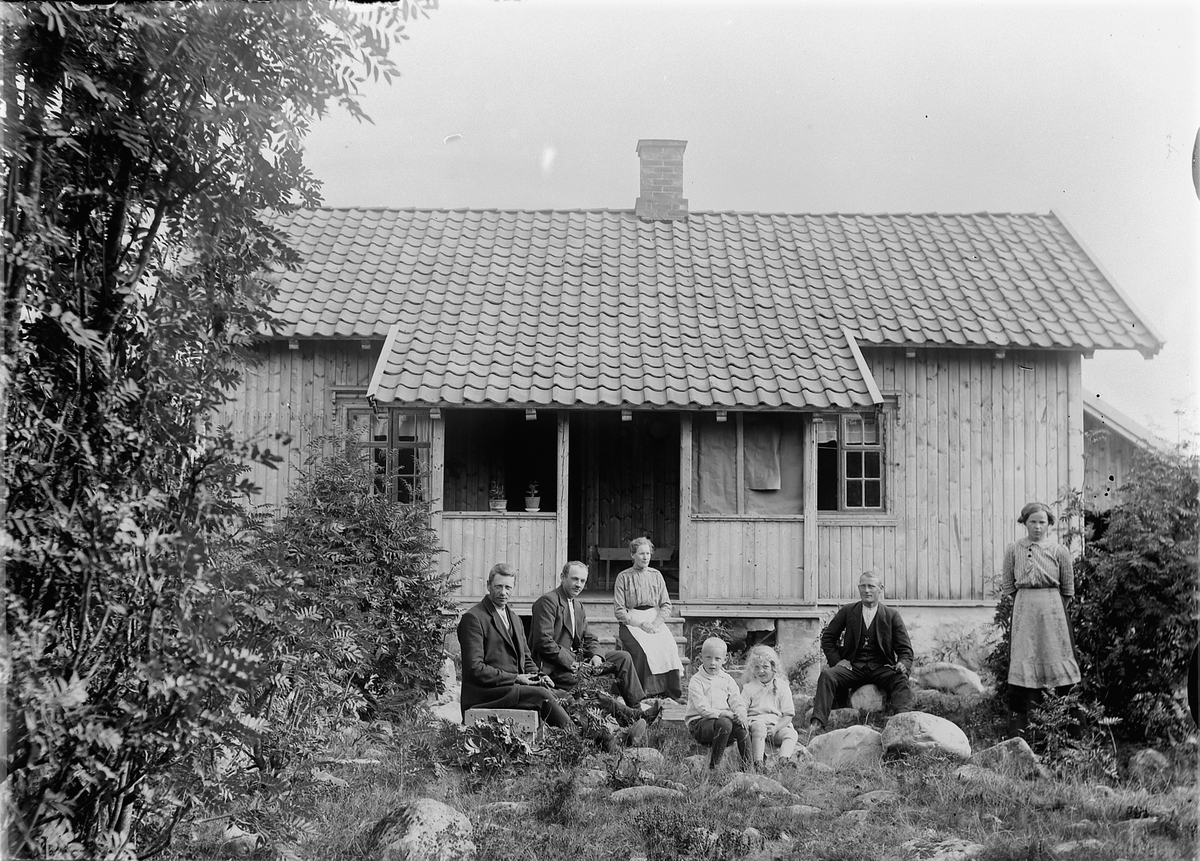 Tre menn, to kvinner, og to barn foran et hus. 