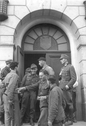 Hamar, fredsdagene i mai 1945, Østregate 54, Frimurerlosjen var okkupert av tyskerne,  
hjemmestyrkene tar over lokalene fra de tyske soldatene, 
På bilde to er delvis skjult til venstre Tor Kløvstad, Hans Bjørlo med ryggen mot fotografen, og den høye med skyggelue ved døra er Kjell Karlsen.