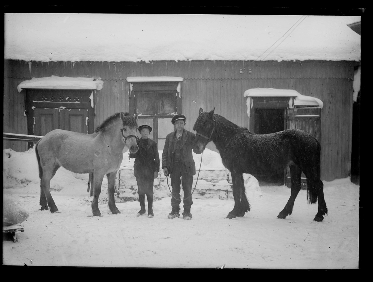 To menn med to hester foran bygning