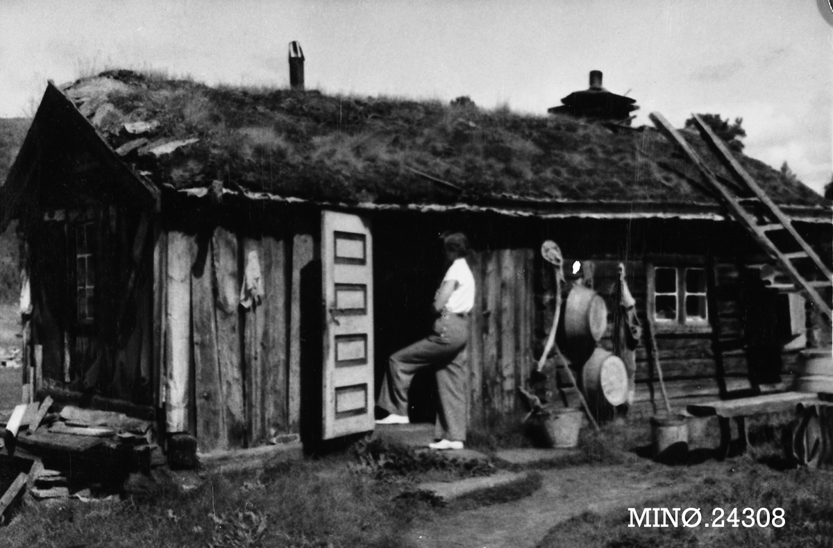 Eldhuset på Tangmoen, Grimsbu, Folldal. Signe Steien i døra.  Bøtter og baljer på veggen ute. 