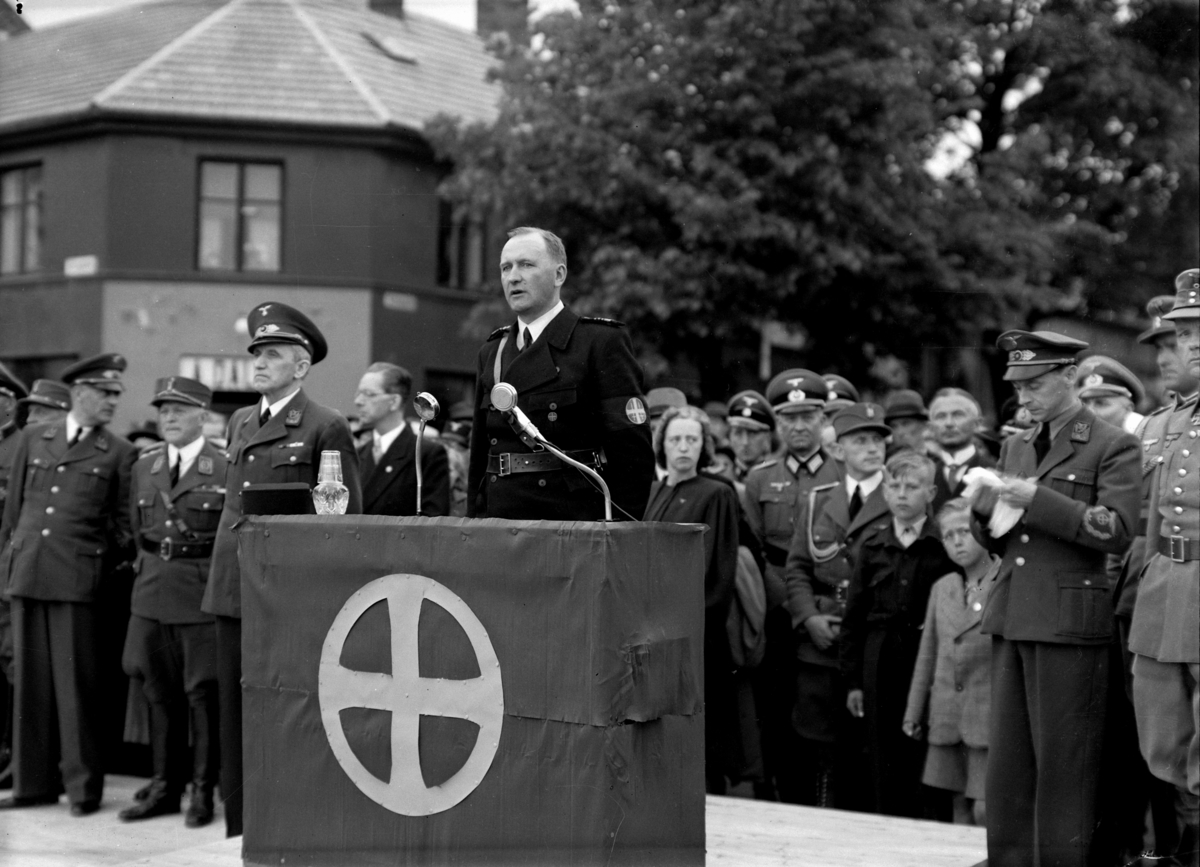 Hamar, Stortorget, Nasjonal samlings jonsokstevne på Hamar i juni 1942, oppstilling på Stortorget, talerstol i Kirkegata, landshirdsjef Oliver Møystad  taler holder tale på Stortorget.
Mannen til høyre i norsk uniform, og med et manuskript i hendene, var statsråd i Quislingregjeringen og propagandasjef i NS, Gulbrand Lunde. Nr. 2 fra venstre er general Carl Frölich Hansen som var leder for arbeidstjenesten AT.
