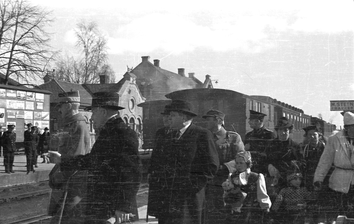 Hamar stasjon, 9. april 1940. Kongefamilien og regjeringen ankommer jernbanestasjonen, fremst går Kong Haakon VII, fulgt av fylkesmann Knut Nordanger, nr tre stortingspresident Carl Joachim Hambro  og Kronprins Olav, prinsesse Astrid prins Harald, barnepike Signe Svendsenog bak politimester Reidar P. R. Beichmann.