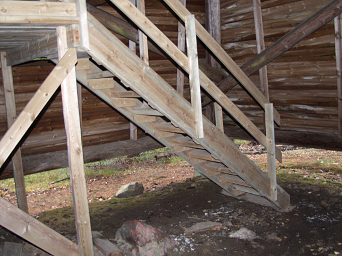 Skogbrannvakttårnet på Hauknesfjellet i Rømskog i Østfold.  Fotografiet ble tatt i forbindelse med oppmålingsarbeid da Norsk Skogmuseum begynte å arbeide med planer om å bygge en kopi av tårnet på museumsområdet i Elverum. 

Tårnet på Hauknesfjellet ligger 335 meter over havet med fin utsikt over vide skogtrakter.  Det første tårnet på dette stedet ble reist i 1909, det neste i 1928.  Det avbildete tårnet skal etter informasjon i forsikringsselskapet Skogbrands arkiver å dømme være bygd i 1953.  Det er reist på et skjellett av stolper (rundtømmer) som er kledd med rødmalt horisontal bordkledning (vestlandspanel).  I den øvre delen av tårnet er det innredet to rom - et oppholdsrom med utvendig balkong på fire sider og et overliggende utkikksrom under en takhatt med vinduer i alle himmelretninger.  Dette fotografiet er tatt inne i tårnfoten.  Det viser den nederste delen av trappa, som fører fra bakken og opp til ei luke i golvet på oppholdsrommet ovenfor.  Bildet viser den nederste trappedelen og deler av første repos, sett fra døråpningen på fasaden mot sør. 