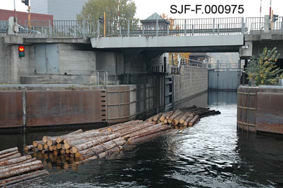 Skien sluse, sett ovenfra eller i strømretningen.  Fotografiet er tatt fra Hjellevannet, mot innløpet til slusene, gjennom øvre sluseport.  Fem bunter er i ferd med å sige mot det øvre slusekammeret.  Ved bildets øverkant skimtes ei vegbru som kunne heises opp når det gikk høye båter gjennom slusa.  Ved tømmerslusing kunne imidlertid trafikken gå uforstyrret.  I bakgrunnen, under brua, skimtes vaktrommet til slusevokterne. 