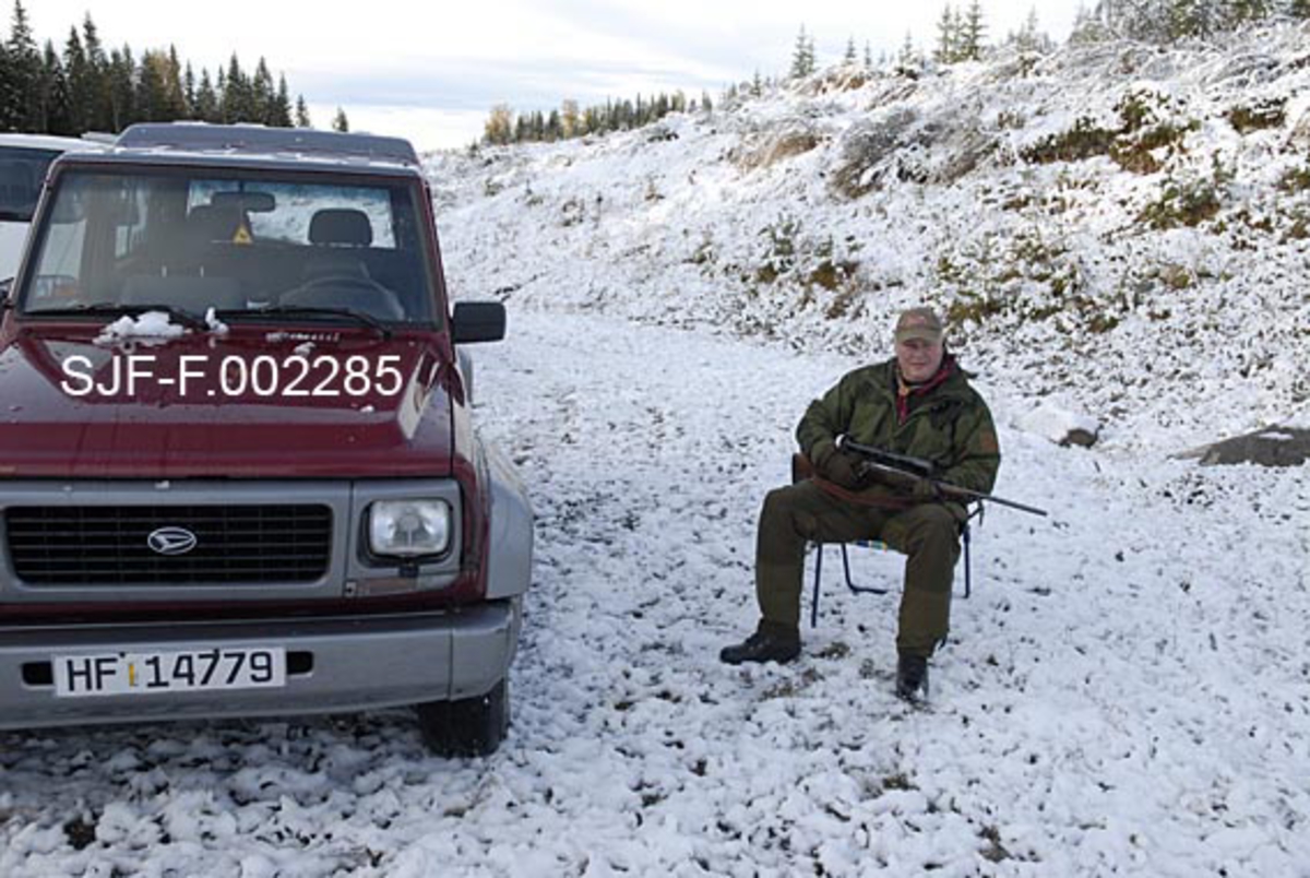 Elgjeger Arnt Svendsberget, fotografert på elgpost under jakta i Tørråsen i Åmot i Hedmark høsten 1989.  Fotografiet er tatt etter at det var kommet et tynt snødekke i marka.  Arnt hadde satt seg på en campingstol like ved bilen sin, en Daihatsu-modell.  Jegeren var kledd i et tidstypisk jaktantrekk.