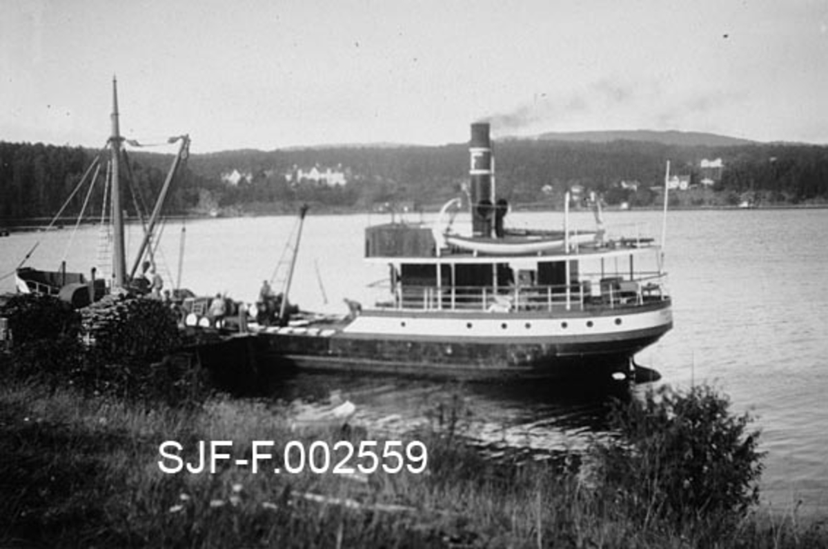 Dampbåten «Farmanden» fra Drammen, fotografert utenfor kaia til Schwencke & Co's Eftf. på Børsholmen i Asker.  Båten hadde stålskrog som i hovedsak var malt i en mørk farge, riktignok med unntak av blant annet koøyefeltet på det overbygde akterdekket.  På det åpne fordekket, mellom kranene forut og styrhuset lå en delt tønner, som antakelig var lastet om bord fra Børsholmen.  Her hadde nemlig Schwencke & Co. en fabrikk som produserte bek og andre tjærebaserte produkter.  På kaia skimter vi et par digre vedstabler.  Veden var viktig for å oppnå nødvendig varme i retortovnene ved industrianlegget.