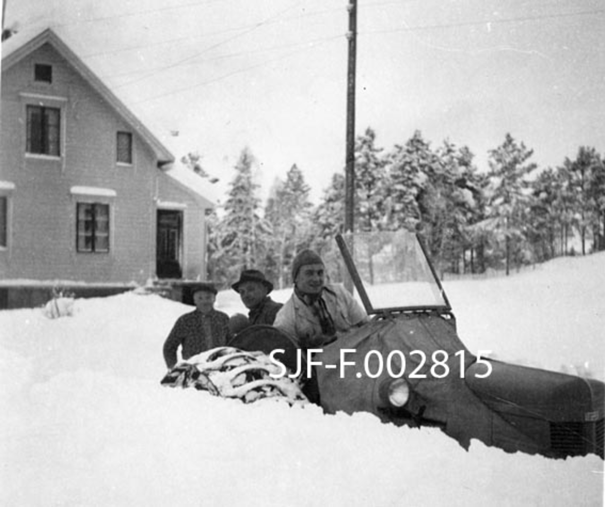 Traktor (Ferguson Gråtass) med halvbelter, fotografert under snøbrøyting på Tollås i Bolsøy i Romsdalen i midten av 1950-åra.  Vi ser bare den øvre delen av traktoren, hvilket gir grunnlag for å anta at snødybden må ha vært over en meter. Traktoren har et presenningtrekk som er lagt over den bakre delen av motorkassa og ei skråstilt frontrute som i noen grad beskyttet føreren mot klimaet, men ingen hytte eller veltebøyle.  Bak rattet sitter Ivar Tolaas.  Bak kjøredoningen ser vi to karer, Nils Tolaas (1893-1973) og Peder Tollås (1897-1972).  Sistnevnte var siste husmann på Tollås.  Han brukte plassen Haugen og drev dessuten litt som skomaker.  Bak dem igjen, til venstre i bildet, ser vi gavlveggen og sideinngangen til våningshuset på Tollås.