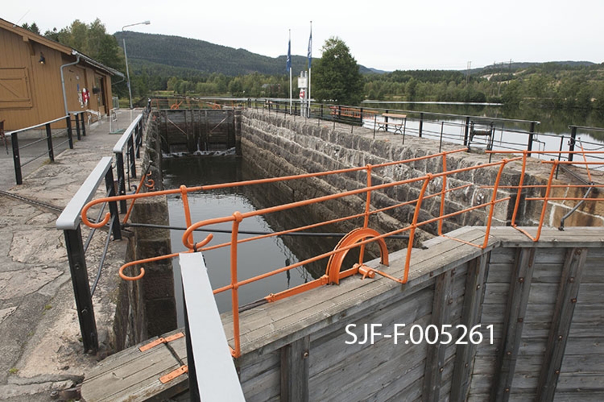 Slusekammeret i Lunde sluse i Bandak-Norsjø-kanalen i Telemark.  Fotografiet er tatt fra slusekammerets sørøstre hjørne.  Slusekamrene i denne kanalen er bygd for å skape passasje for fartøyer som var inntil 31, 4 meter lange, 6, 6 meter brede og stakk inntil 2, 5 meter djupt.  De var omgitt av fugete murer av hoggen naturstein, og hadde porter av tre med smijernbeslag.  Botnlukene ble åpnet ved hjelp av spaker oppå portene, og når portene skal åpnes brukes spett i perforerte skinner på murkronene.  I 1970- og 80-åra argumenterte Skiensvassdragets fellesfløtningsforening, som var den største brukeren av kanalen, for at slusene måtte få glatte vegger og porter med motoriserte åpne- og lukkemekanismer.  Dette kravet ble innfridd ved Skien og Løveid sluser, men aldri i Bandak-Norsjø-kanalen, som ble drevet videre som «museumskanal». 