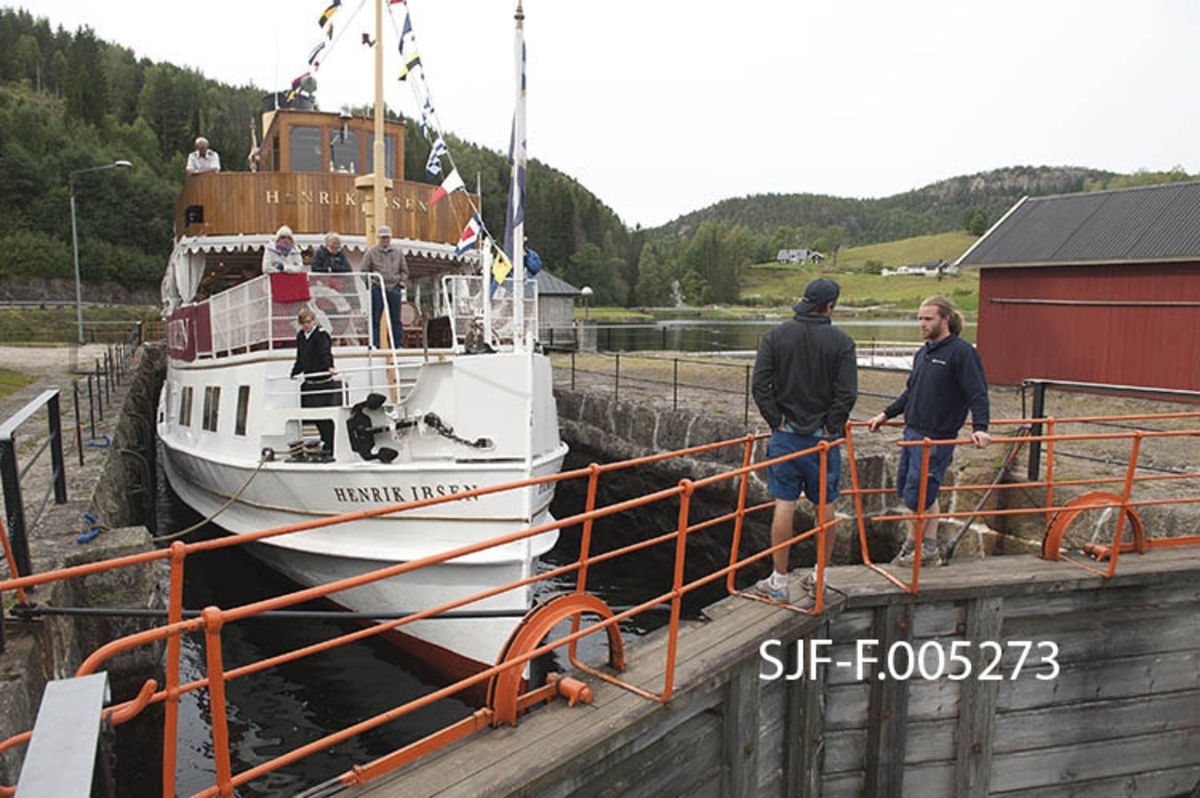 Turistbåten «Henrik Ibsen» i Kjeldal sluse i Bandak-Norsjø-kanalen.  Sluseanlegget ligger i Nome kommune.  Her er det ett slusekammer, som utlikner en høydeforskjell på tre meter mellom ovenforliggende og nedenforliggende del av vassdraget.  Sluseanleggene betjenes i 2012 av to slusevoktere som reiser foran rutebåtene i bil.  Her ser vi karene på brua over nedre sluseport. Båten går i rute mellom Skien by og Dalen i Tokke, innerst ved Bandakvatnet, en distanse på 105 kilometer.  Henrik Ibsen er det største, raskeste og mest luksuriøse skipet i Skiensvassdraget.  Fartøyet er opprinnelig bygd som dampskip ved Eriksbergs Mekaniska Verkstad i Gøteborg i 1907 for Styrsö-bolaget.  Derfor fikk båten først navnet DS «Styrsö».  Under dette navnet gikk fartøyet i mange år som rutebåt i Gøteborg-skjærgården.  Etter en periode som charterbåt på den svenske vestkysten ble Styrsö oppkjøpt av Skien Dalen Skipsselskap AS og satt trafikk i Skiensvassdraget i forbindelse med Bandak-Norsjø-kanalens 100-årsjubileum i 1992.  Her fikk båten navnet «MS Henrik Ibsen», etter den berømte forfatteren med tilknytning til Skien og en hurtiggående dampbåt som gikk i vassdraget tidig på 1900-tallet.  I perioden 2009-2011 ble skipet restaurert med sikte på at det igjen skulle framstå som det hadde gjort da det var nytt.  Etter dette har fartøyet vært driftet av Norwegian Hospitality Group AS, som eier Telemarkskanalen Skipsselskap AS.  Selskapet disponerer også det tradisjonsrike drakestilhotellet på Dalen, som er endestasjon for båtruta.  Sesongen for kanalbåtene starter vanligvis i midten av mai og varte til andre halvdel av september. Seilasen mellom Skien og Dalen med turistbåten Henrik Ibsen tar cirka ni timer. MS Henrik Ibsen har aller rettigheter og det er restaurant ombord med daglig servering av frokost og lunsjretter.  Båten går opp den ene dagen og ned igjen den neste.  Turistbåten MS Victoria går ned til Skien den dagen Henrik Ibsen setter kurs for Dalen, og går ned igjen den dagen den andre båten er på veg opp. 
