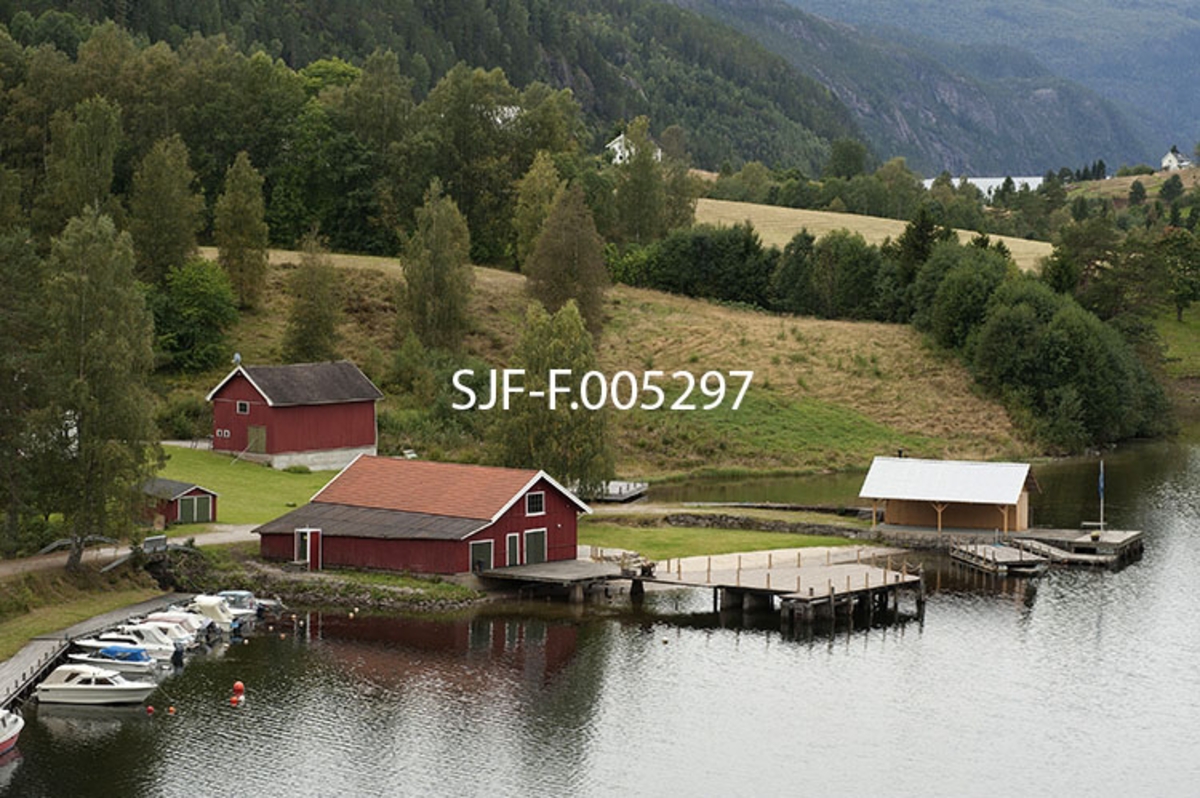 Strengen i Flåbygd (Nome kommune i Telemark), sett fra vegen langs det trange sundet med samme navn.  Ved Strengen var det brygge, og her hadde dampbåten Axel, som slepte tømmer på Vestvannene (Bandak, Kviteseidvatn og Flåvatn i Vest-Telemark) sin base.  I dag går mesteparten av trafikken i dette området på fylkesveg 107, hvor det i 1964 ble bygd ei buebru i armert betong over Straumen.  Brygga med godshus er imidlertid intakt, og området nedenfor brukes også som fortøyingssted for fritidsbåter.  Fotografiet er tatt fra den nevnte brua, noe som har gitt bildet et visst fugleperspektiv. 