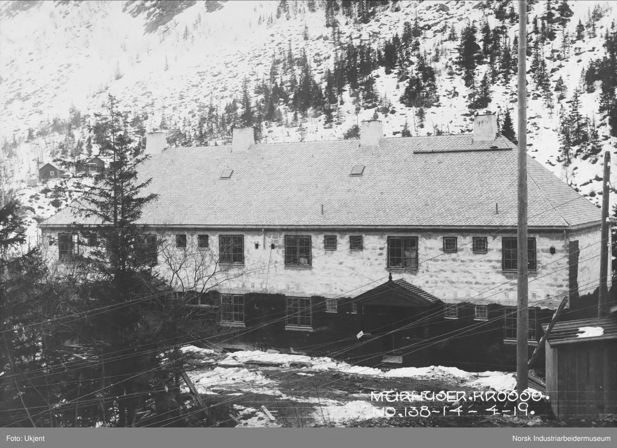 Murhusbebyggelsen på Krosso under oppføring. Bolighus ferdig oppført, skiferstein på taket. Bebyggelse på sørsiden av juvet i bakgrunnen.