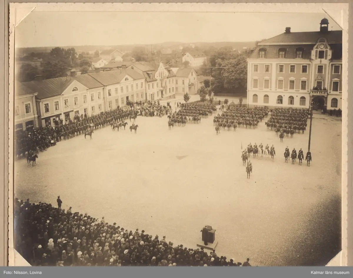 KLM 15433. Fotografi, i grått omslag av kartong. Mått: H 24,5 cm, Br 31 cm. Tre olika fotografier föreställande Kungliga Smålands Husarregementes paradering och gudstjänst på Eksjö torg 1923.