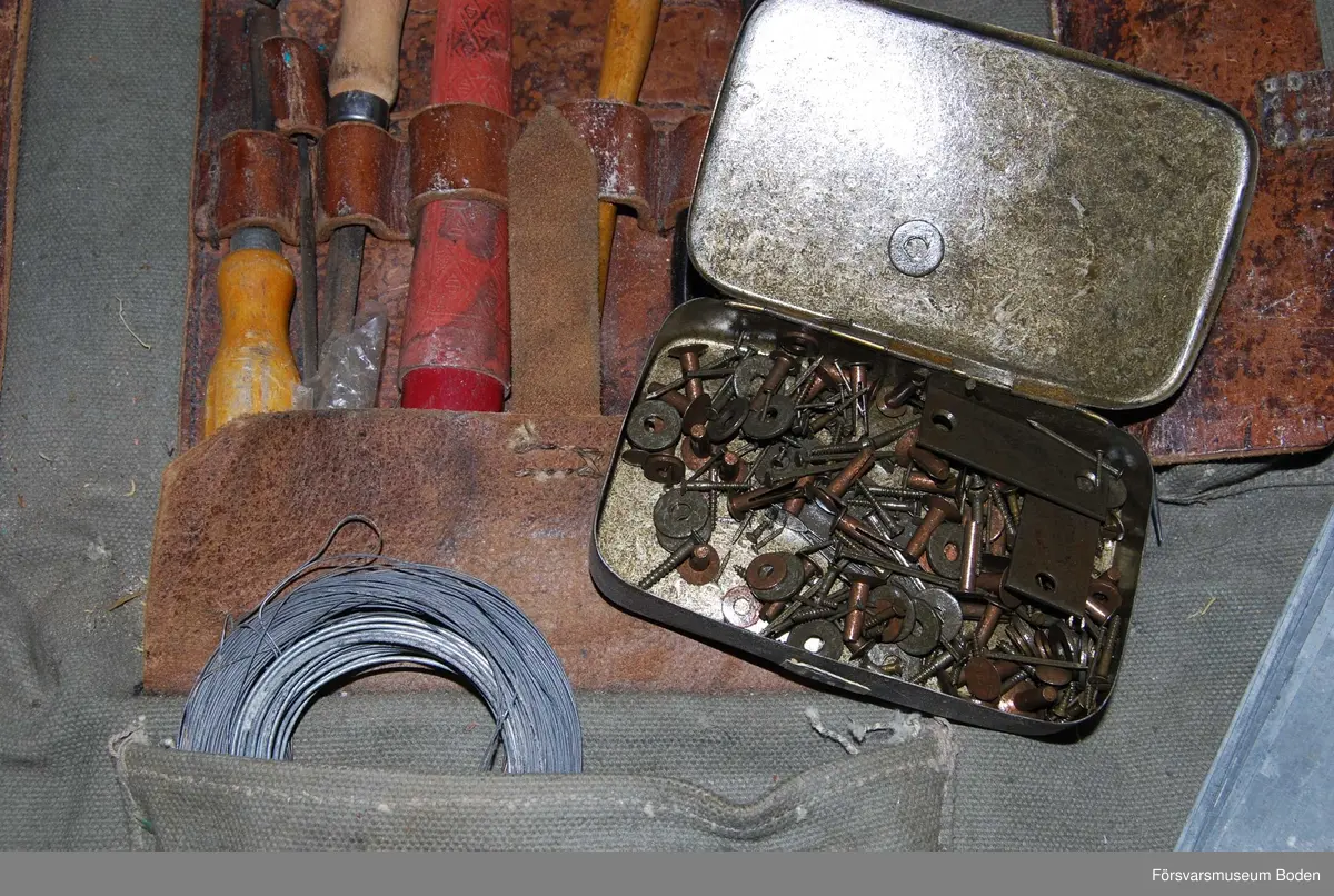 Verktygssats i väska av grågrönt textilmaterial med axelrem. Innehåller även förbrukningsmateriel som bleckplåtar, wire, nitar o.dyl. Väskan vikes upp och har hållare för verktyg i centrum samt tre fickor med lock. Materielnummer M8740-101110 enligt bifogad satslista.
