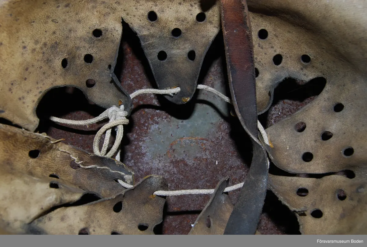 Kanten omvikt mot insidan. Inredning med aluminiumband, stämplat 1938. Rester av grön färg på insidan. Dekaler på båda sidor, varav endast rostkonturerna syns på den vänstra sidan. Storlek 59