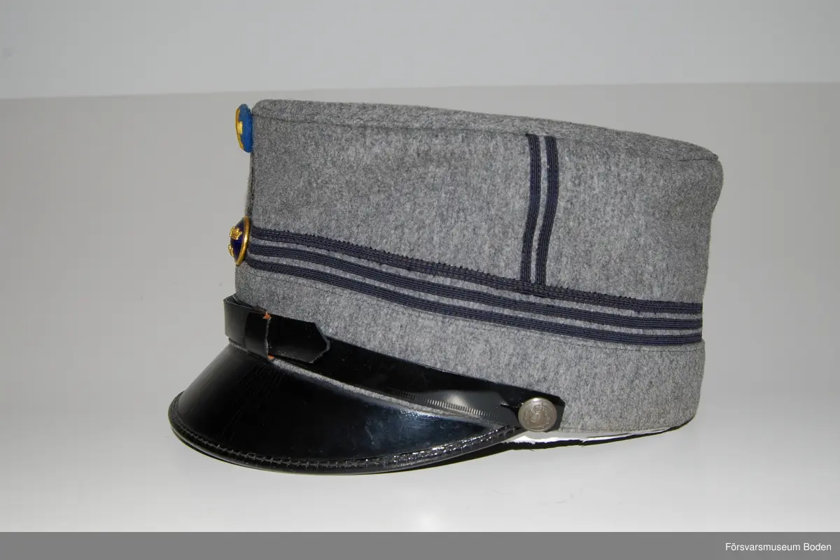 Ljusgrått kläde med tre smala band av blått kläde runt mössan betecknande kapten. Framtill mössmärke m/1865 i blå emalj samt upptill landstormsmärke m/1926 med gult broderat kors på blått kläde. Mössremmen fäst på sidorna med landstormens knapp modell mindre. Buren av fil. dr Arvid Moberg.