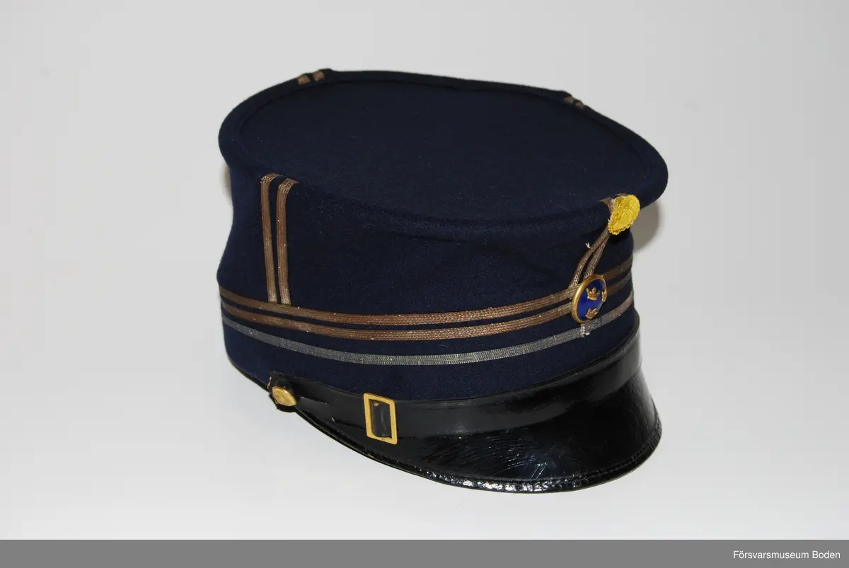 Mörkblått kläde med tre smala silvergaloner runt mössan betecknande kapten. Framtill mössmärke m/1865 med blå emalj för officererare, och ovanför detta gul sidenkokard. Mössremmen fäst på sidorna med artilleriets knapp modell mindre i guld. Buren av C.G. Dahlberg.