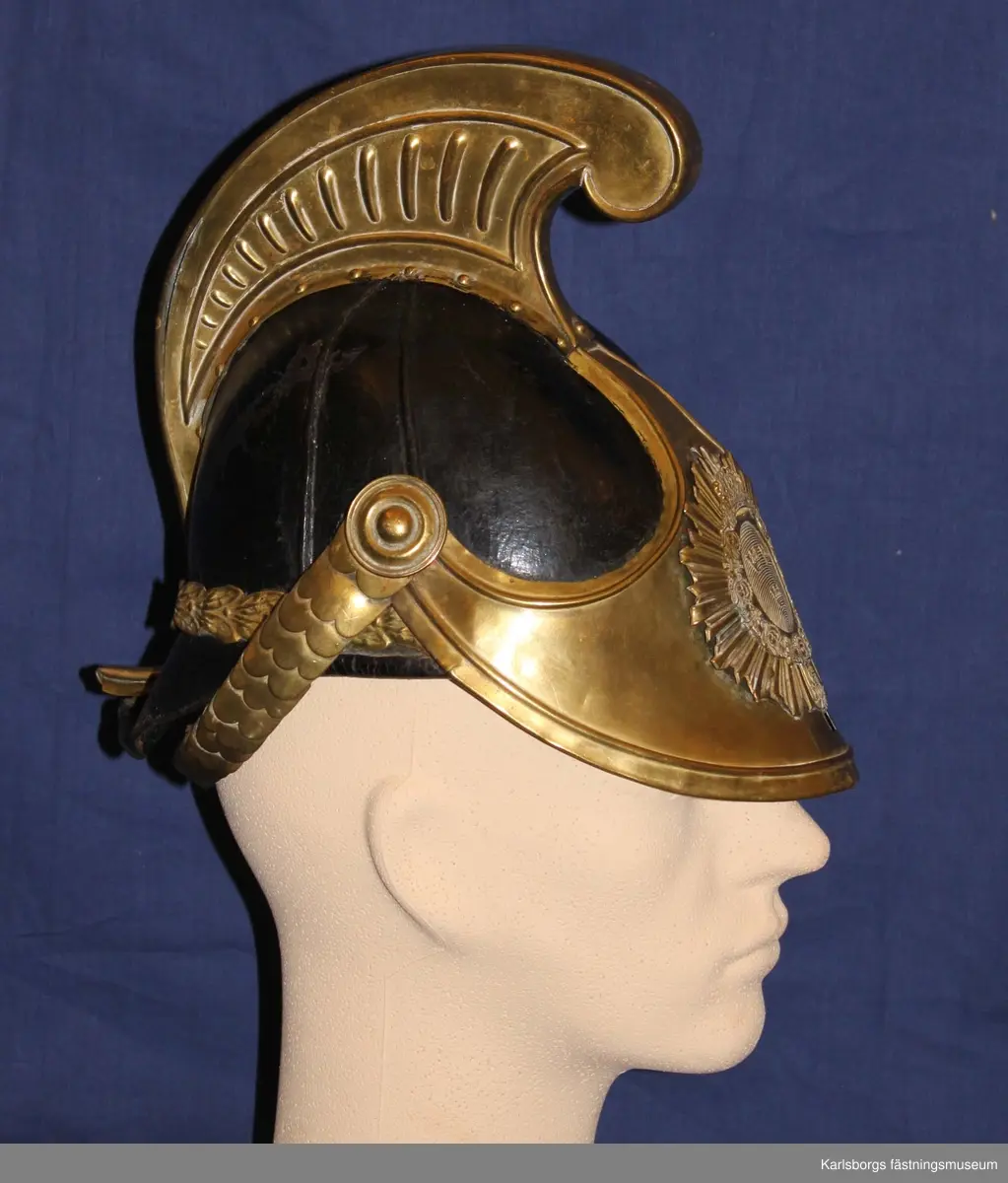 Kask m/1846, tillhörande Kavalleriet, Livregementets dragonkår. Se 6732. Avvikelser: Ingen gul sidenkokard under hakremsknappen, ovanpå kasken finns en plåtdel som går uppåt ca 7 mm och böjer sig i en båge längst fram där plymen sätts fast, kavalleriets vapenplåt.