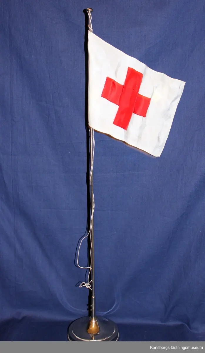 Bordsflaggstång i silver med rödakorsets flagga.