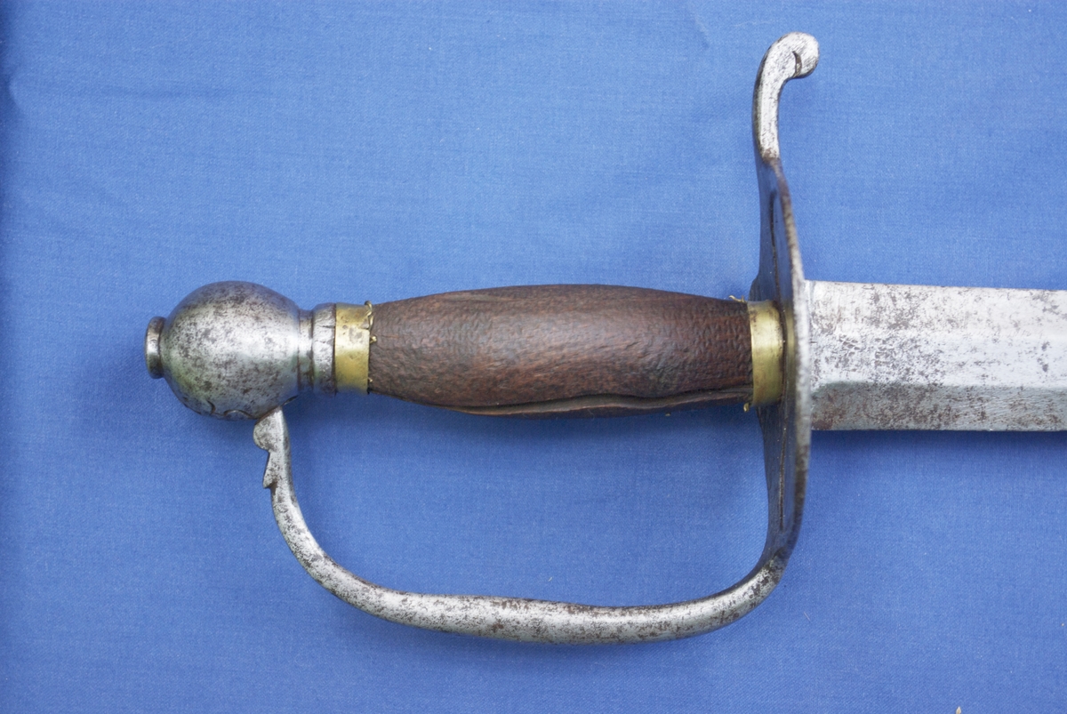 Tveegget sverd med flat klinge og brede egger. Parerplate, bøyle og knapp av jern. Kavle av tre med messingholker rundt endene. På klingen speilmonogram F 4 med krone over. På knappen H N0 5. solid parerplate som går over i en 3 cm lang stang med nedbøyd ende. Bøylen er en fortsettelse av platen og er svakt rundet og stukket inn i knappen. Eggformet knapp med spissen ned, knott på toppen der tangen er klinket. Kavlen har hatt surring av tvunnet messingtråd, rester av tråd sitter igjen under messingholkene. Klingens egg har huggsår.