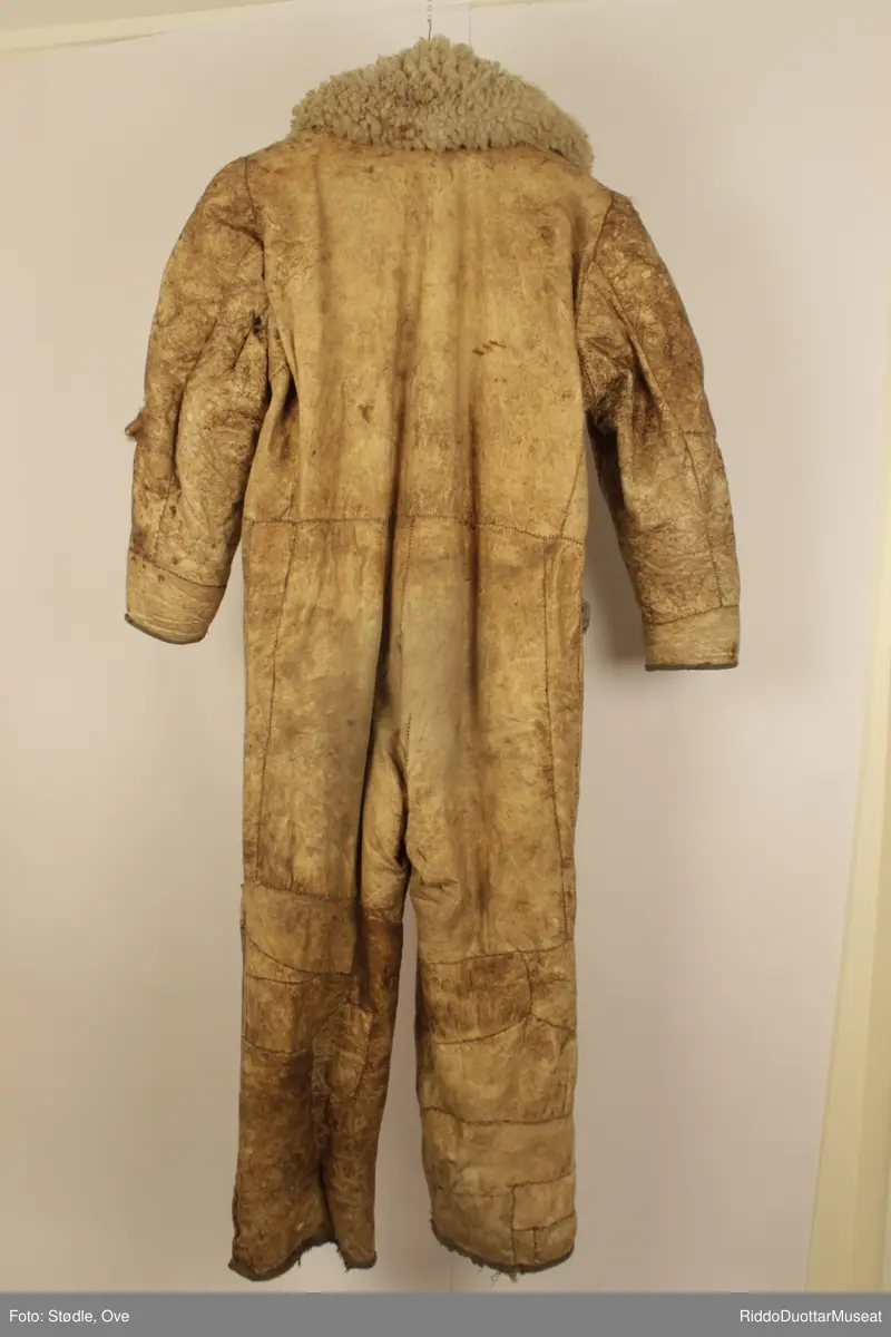 Hel dress, 173 lang. Sydd av saueskinn og sannsynligvis storfeskinn, med hårsiden innover.  Kragen er sydd av saueskinn med ullsiden ut. Glidelås-lukning. Ligner en gammel flydress. Lomme øverst på høyre lår er sydd av grått stoff, og har en rød og en brun knapp.