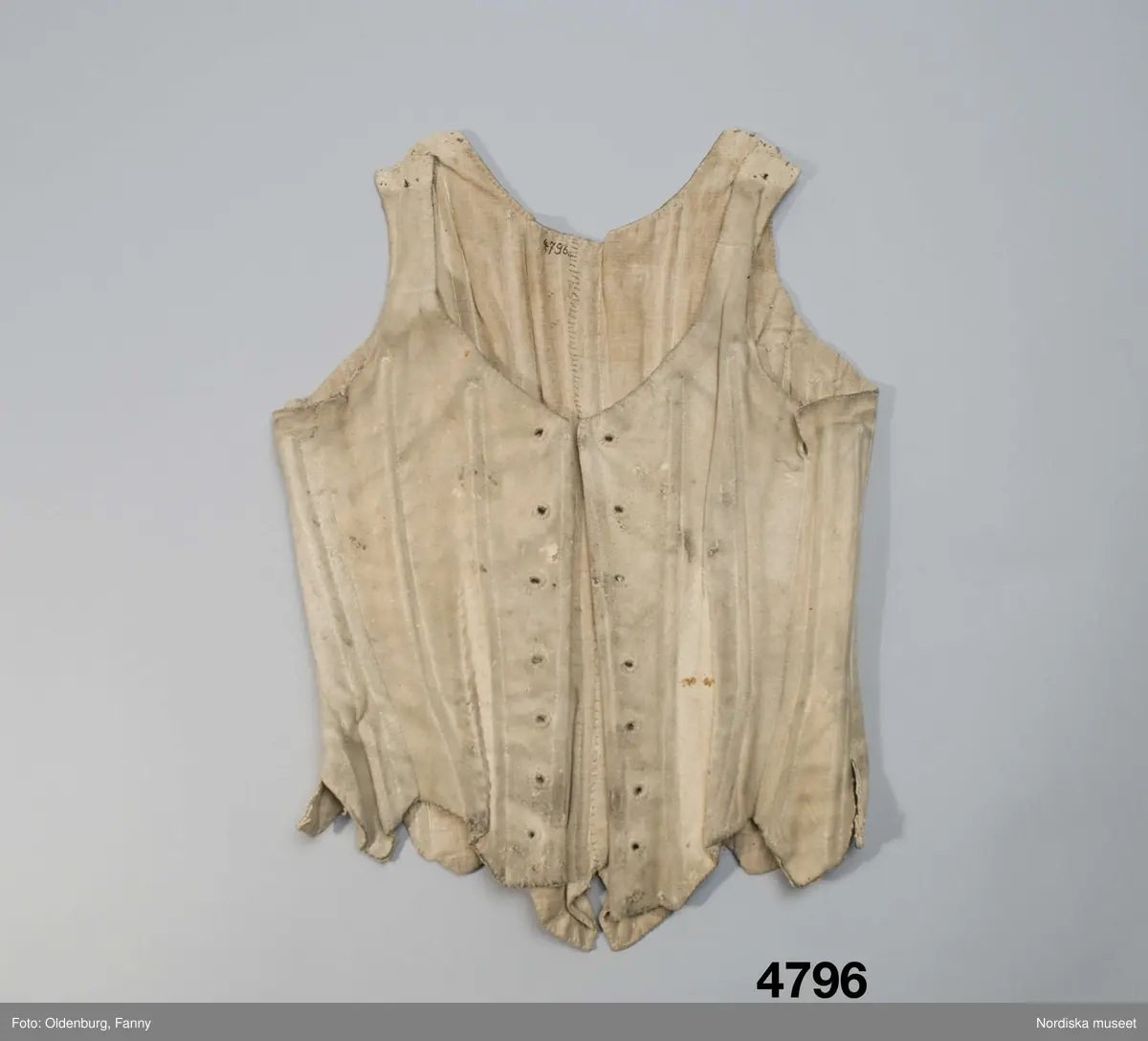 Snörliv av ljust sämskskinn. Skuret i 10 smala delar med 20 kanaler för styvnader av valben. Axelbanden öppna med ett snörhål i var ände för reglering av längden medelst knytband. I framkanterna snörning med ursprungligen 8 par snörhål kantsydda med lintråd. Helfodrat med oblekt linnelärft.
Har förändrats för att bli mindre. Dels har minskningen gjorts mitt bak med en ny söm, dels har framkanterna vikts in och sytt fast mot fodret och 8 par nya snörhål har prylats och kantsytts. På framstyckena finns även sekundärt gjorda insyningar som sedan sprättats upp.
Snörliv med valben var dyrbara och kan ha gått i arv från t.ex. mor till dotter och då sytts om för att bli smalare.
Anm. Solkigt och bitvis slitet invändigt med hål vid kanalerna där valben syns genom hålen. Flera valbenen saknas också. Troligen har det från början varit järntenar i framkanterna vid den ursprungliga snörningen.
Har enl. förmedlaren tillhört prostinnan Sara Hazelius i Bergsjö, Hälsingland. Sådana snörliv bars inte av allmogekvinnorna.
Sara f. Eneroth 28/9 1726 var dotter till kyrkoherde Pehr Eneroth i Svenljunga, Älvsborg. Hon gifte sig 1756 med sedemera prosten i Bergsjö Pehr Hazelius och fick 8 barn 1757-1768. Hon dog 1795.
Läs om snörliv B.Hammar/P.Rasmussen: Underkläder, Signum förlag 2008 
/Berit Eldvik 2008-05-21