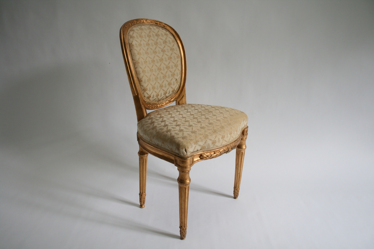 Forgylt stol, med oval rygg, kanelerte bein. Trukket med mønstret trekk i en beige-rosa farge.
Louis seize.
En av to like stoler.