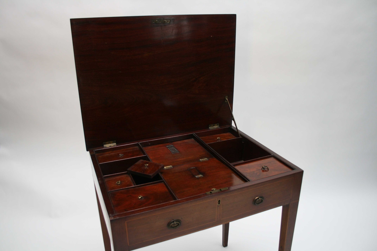 Polert mahognibord med intarsia. Rektangulær plate, avsmalende bein og to falske skuffer i sargen. Bordplata kan slås opp, og under er det et lite skyvespeil og 9 små rom, 6 rom har lokk.