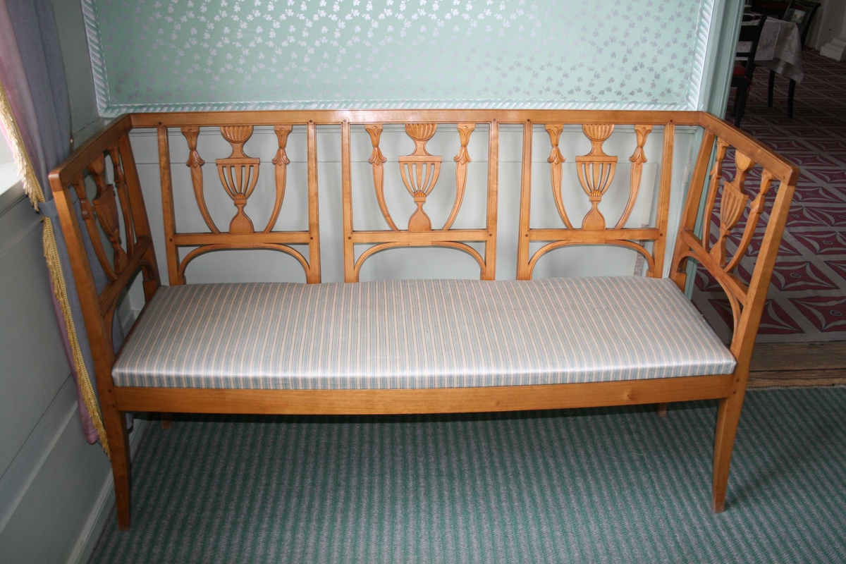 3-sete bjerkesofa i empirestil med ryggbrikke utformet som en urne. Løst sete med stripete trekk, lys blått og lys grått like striper med en mørkere grå tråd innimellom, håndvevet.