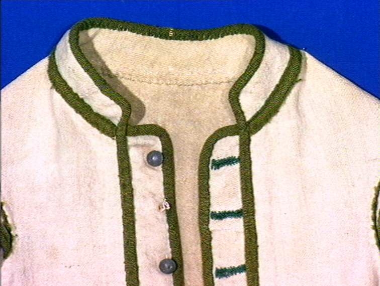 Hvit kjole av ull med grøn dekor av ull.
Midjen bak er markert med to garn dusker.