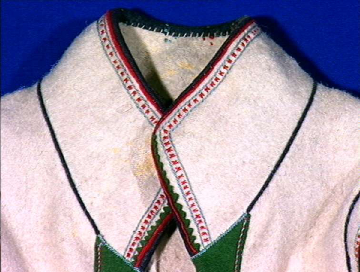 Hvit mannskofte av vadmal med gønne kanter av klede (oppslag).
Nedrekanter, ermebryninger og halskrage har dekor av rød korstign avgrenset av blått konturstign (ullgarn).
Halskrage ha kanting av svartklede med tittkant av rødt klede.
Ermer har et ca. 6,5 cm bredt belegg av grønn klede kantet med rødt klede.