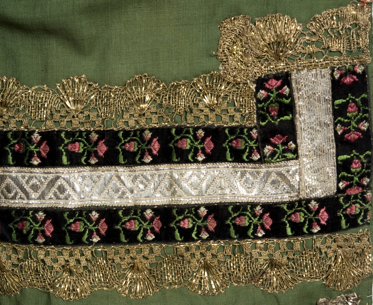 Grønt forkle av ull med dekor av metallblonder og bånd.