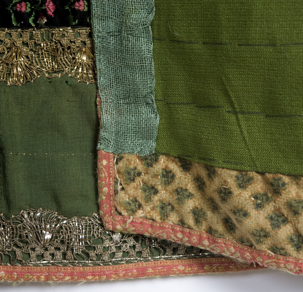 Grønt forkle av ull med dekor av metallblonder og bånd.