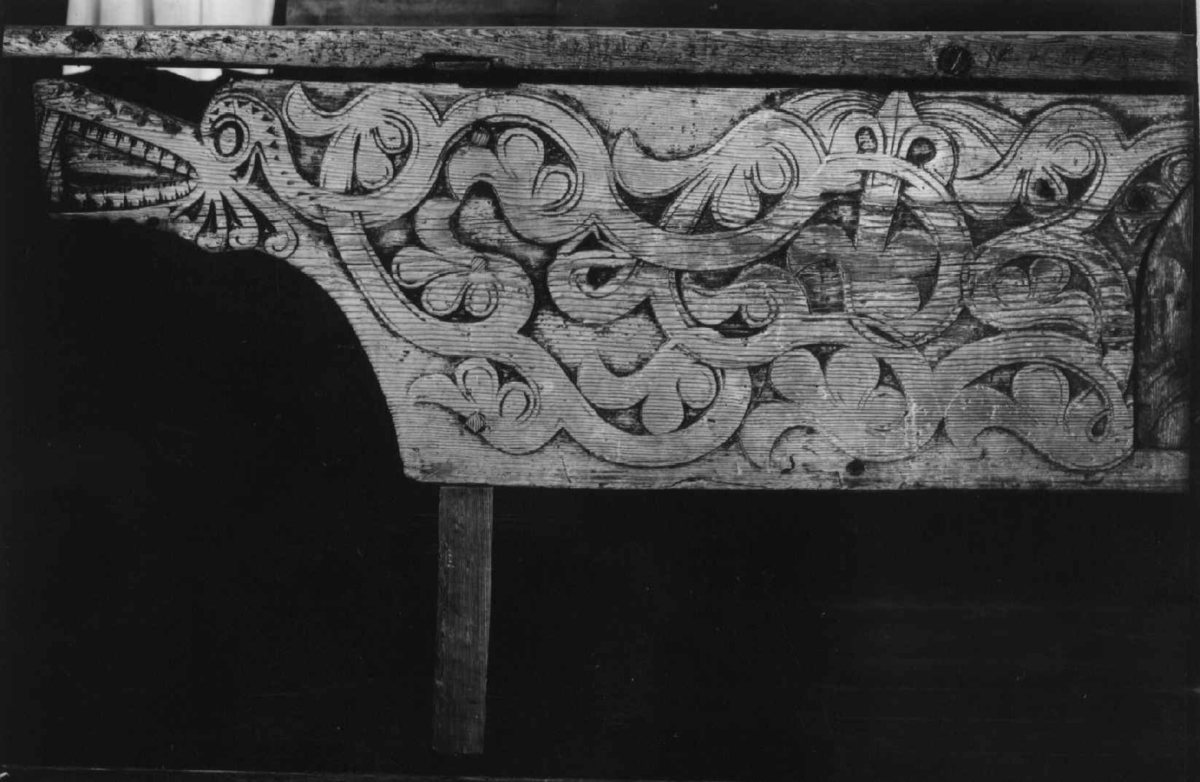 Langbord med forvaringsrom bak høye sarger. Fremsarg er med heldekkende flatskurd ranker og drageornamentikk samt en luke til forvaringsrommet. 