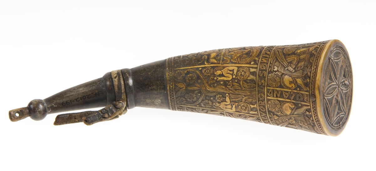 Krutthorn med flat, ornamentert bunnplate i tre. Ornamentikk på horn i form av 11 stk motivfelter omgitt av bårder med tekst. Motivene er: Adam og Eva ved Kunnskapens tre, Samson og løven, Daniel og dragen. Avbildede som rytterfigurer: Angolan, Karvel, Vidrik, Tidrik, Roland, Otvel, Burman og Olger Danske.