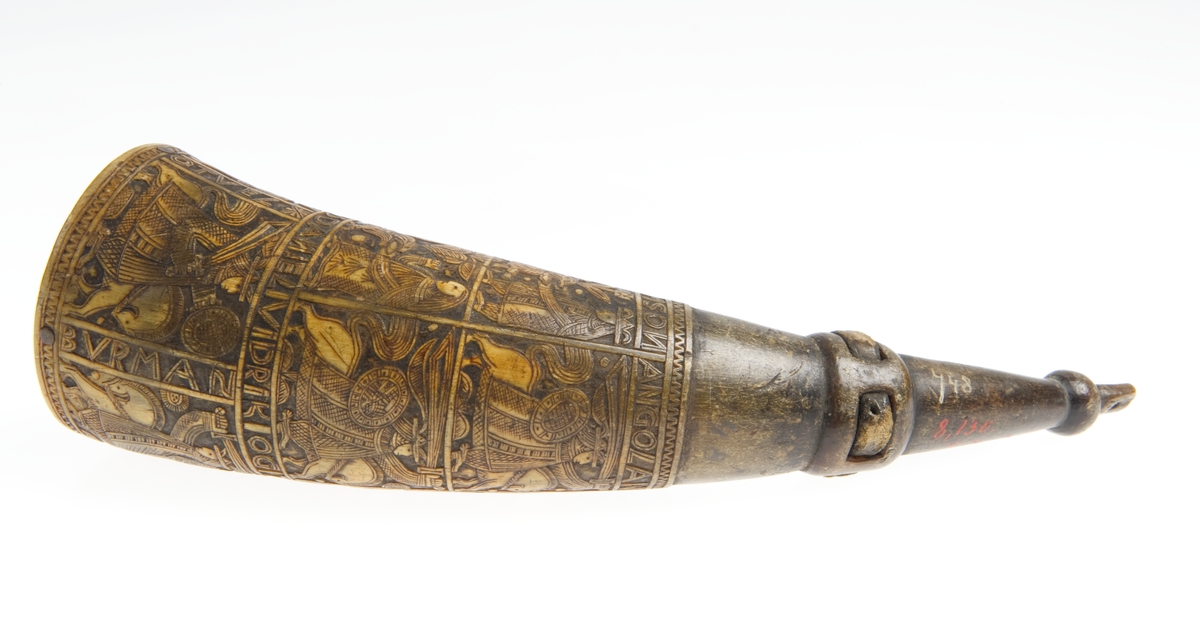 Krutthorn med flat, ornamentert bunnplate i tre. Ornamentikk på horn i form av 11 stk motivfelter omgitt av bårder med tekst. Motivene er: Adam og Eva ved Kunnskapens tre, Samson og løven, Daniel og dragen. Avbildede som rytterfigurer: Angolan, Karvel, Vidrik, Tidrik, Roland, Otvel, Burman og Olger Danske.