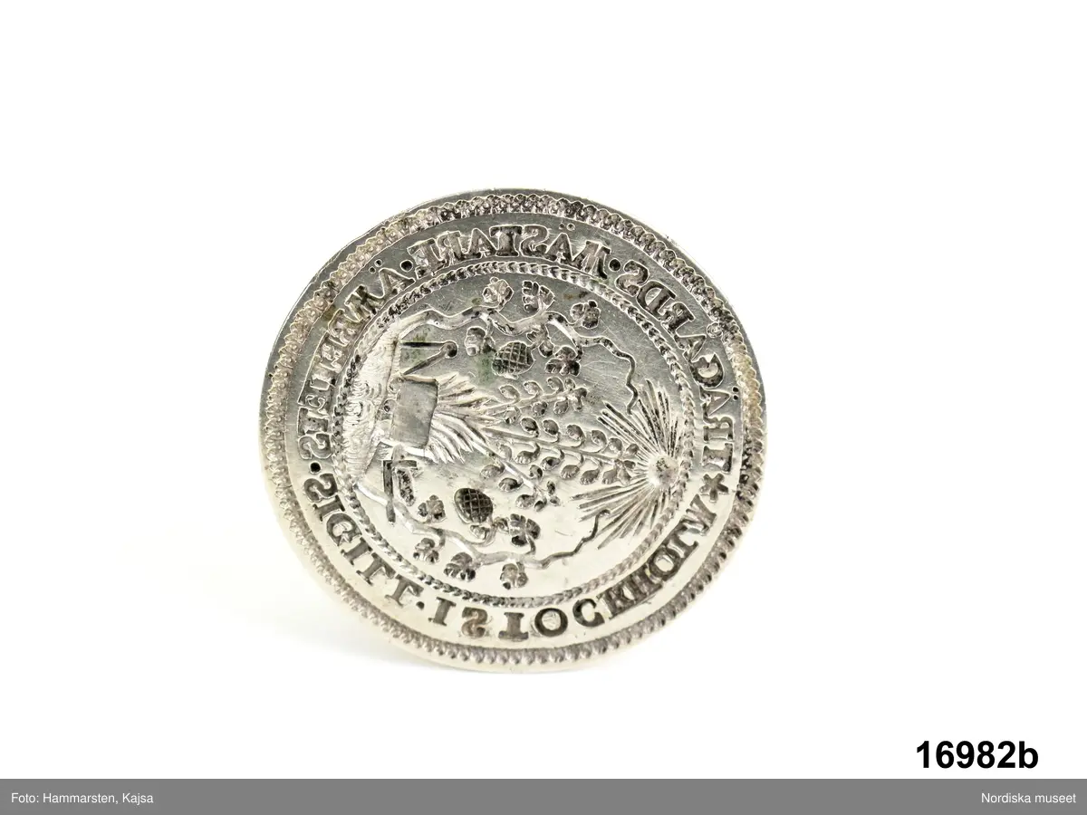 Huvudliggaren:
"a-e Låda och sigillstamp, som tillh. trädgårdsmästarämbetet i Stockholm. a. Låda. b. Sigillstamp af silfver (med lyrformigt handtag af samma metall, upptill afslutadt med ett genombrutet hjärta.) 'Trädgårdsmästareämbetets sigill i Stockholm [ritat: femuddig stjärna]' Inskriften i latinsk stil. H (med handtag) 0,06. Diam. 0,038. I sigillet en blomburk med växter mellan tvänne vinrankor m.m. öfverst en strålande sol, alt inom pärlring. Å handtaget märkt: '1757'. I stämpeln å handtaget läses: 'I.BERG' m.m. som är otydligt. b. Se ill. bil. c-e. 3 st. nycklar. [järn. a, L 13 cm, b. L 11 cm, c. L 11 cm.] Samma ämbetets handlingar se 16.251 a-i. G[åva] af trädgårdsmästarne D. och J. Berggren. 5/4 1877." 

Utdrag ur bilaga:
"Genom herrar trädgårdsmästare David och Josef Berggren har jag denna dag såsom gåfva till Skandinavisk-etnografiska samlingarna emottagit f.d. trädgårdsmästare-socitetens i Stockholm mästerlåda och dödlåda med åtskilliga handlingar och ritningar 16.251; 16.982; 16.983, vilket å samlingens vägnar härmed tacksamt intygas."