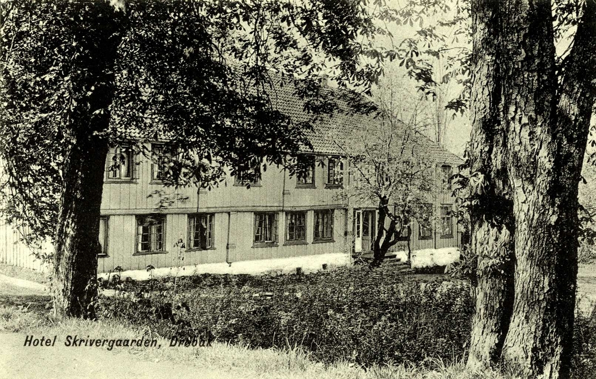 Hotel Skrivergården, Drøbak, Frogn, Akershus. Stor trebygning sett mellom trær mot hagen.