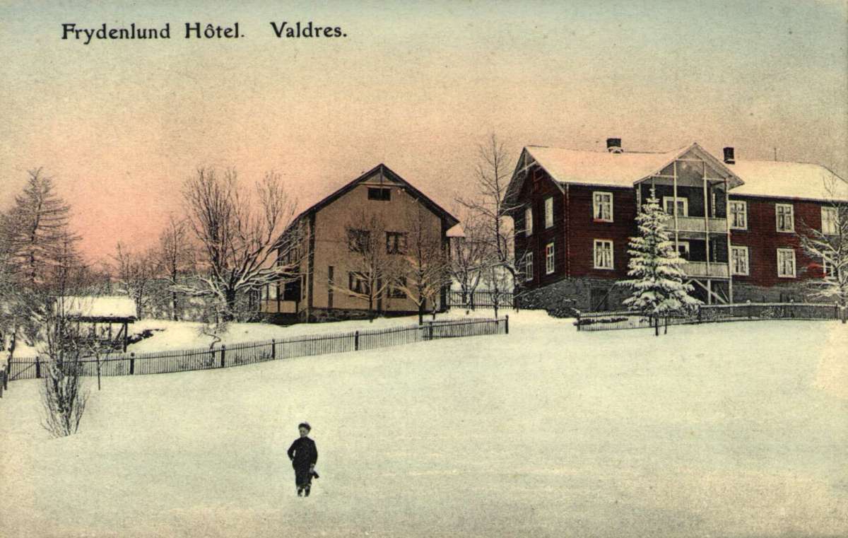 Postkort. En gutt står på snølagt jordet foran Frydelund Hotell, Valdres