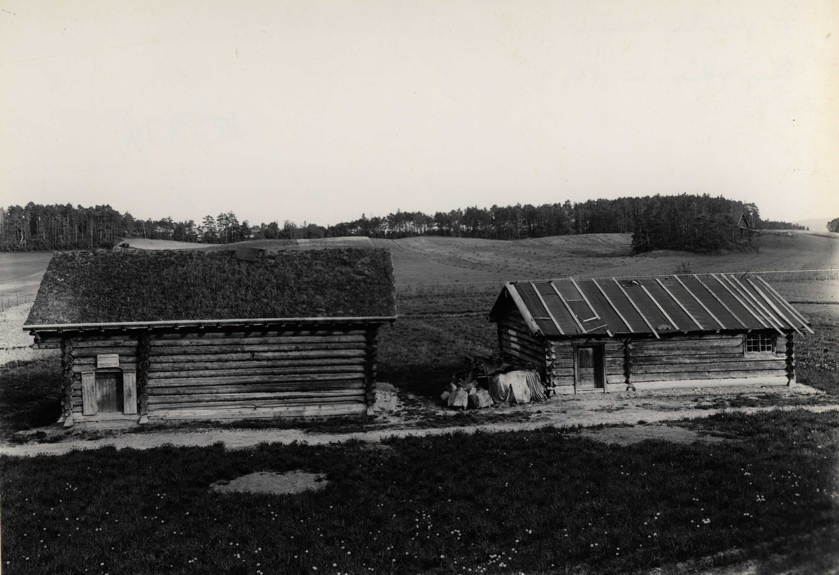 Raulandstua (NF.021) og Grøslistua (NF.022) på Norsk Folkemuseum 1903. Åpne jorder, skog og en låve i bakgrunnen (det som nå er Hallingdal).