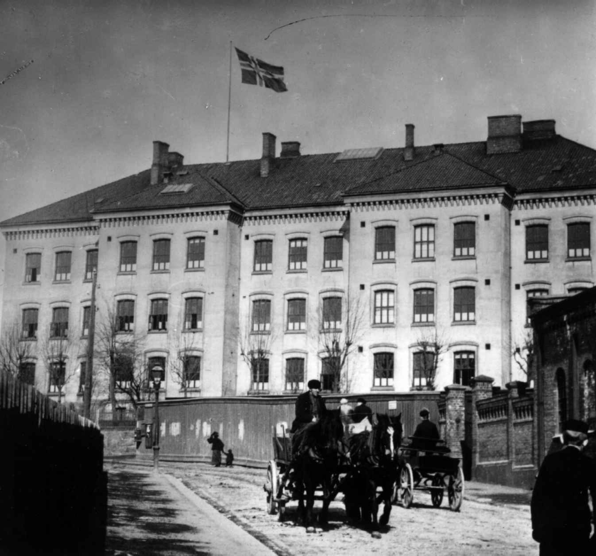 Sagene skole, Oslo ca. 1905. Gatebilde fra Sagene skole med hestekjøretøy i gata. Til 1905-utst. NF.