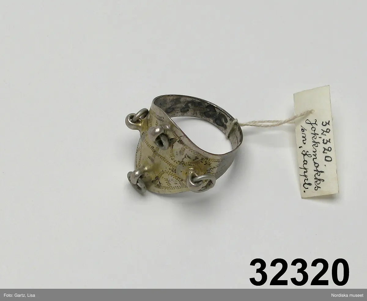 Huvudliggaren:
"Ring fr. Jokkmokks sn. Af silfver. Märkt: '4 L' 'O F.' Ink. af major V. Stål i Stockh. jämte 32.318-32.325. 1/7 1882."