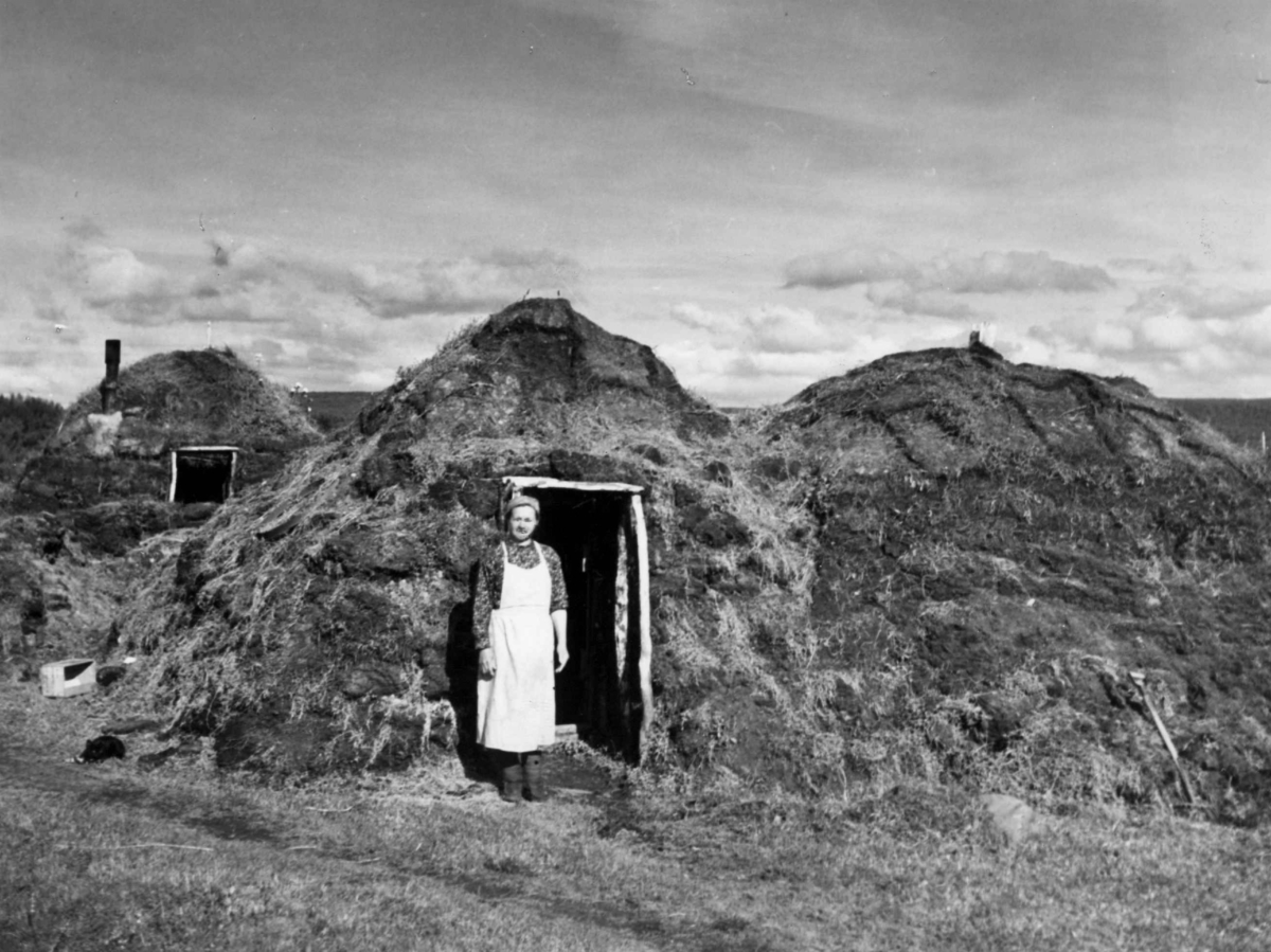 Gammer, en kvinne står i døråpningen i en av dem. Varangsbotten antagelig 1930-årene.