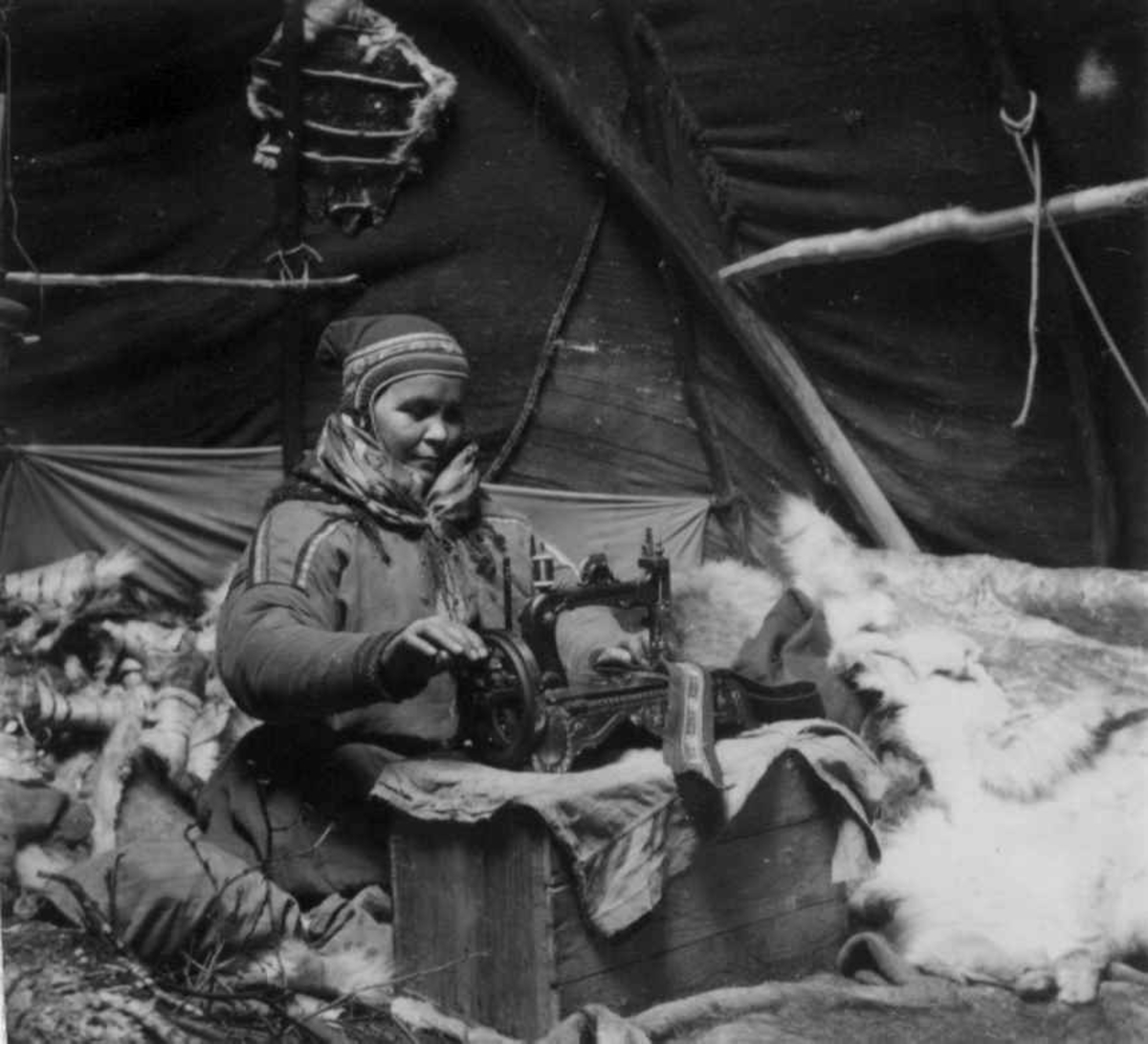 En kvinne sitter i et telt og syr kofte. Kautokeino.
