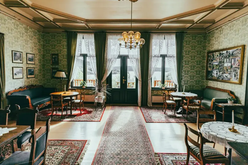 Den grønne salongen på Villa Fridheim. Stor stue med fire sittegrupper, gamle møbler og store vinduer som vender ut mot hagen.