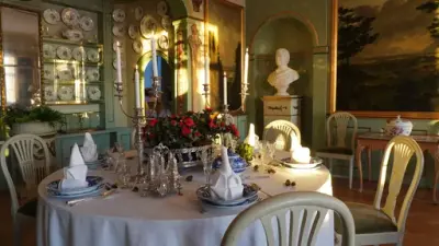 Et dekket bord med en blomsteroppsats med røde blomster i hovedhuset på Bogstad gård. 