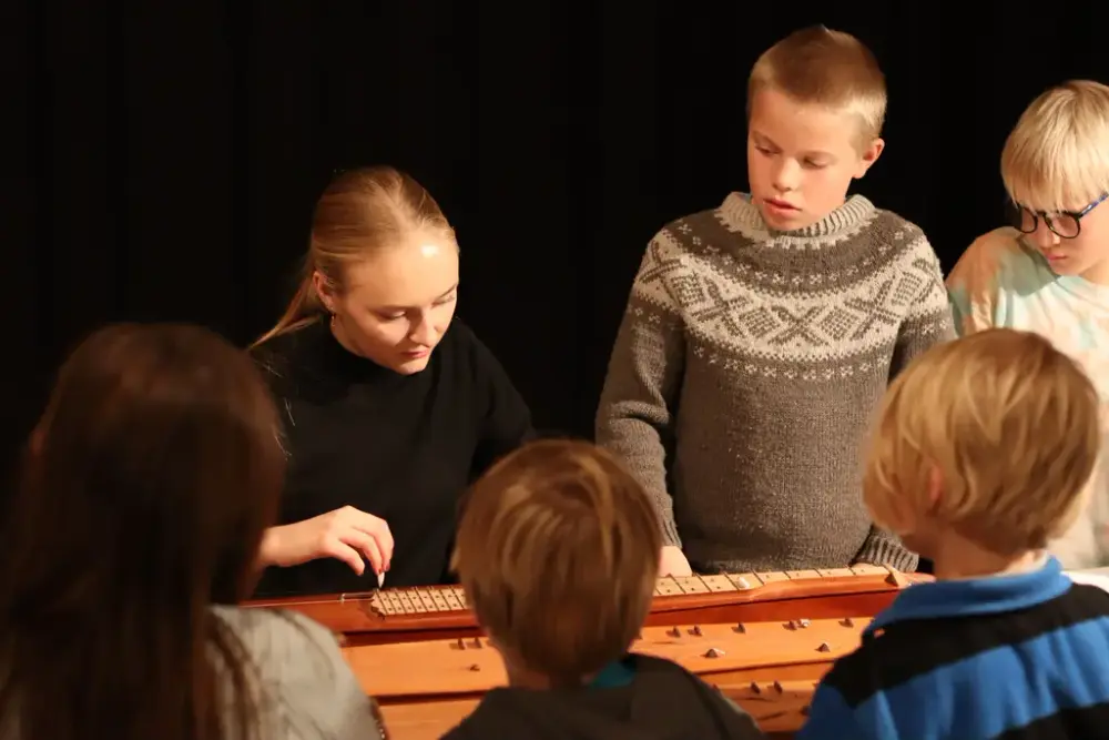 Bilde av Andrea Søgnen som spiller langeleik med barn stående rundt. 