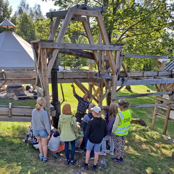 Bilde av skoleelever og museumsvert som viser fram gruvepumpa på Labro. 